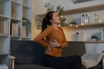 Health Awareness. Woman experiencing back pain while sitting on couch at home.