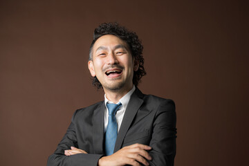 茶色背景でスーツを着た腕を組む笑顔のビジネスマン