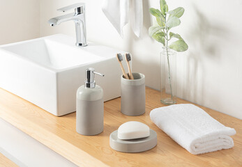 Contemporary eco-conscious bathroom detail, a sleek square white countertop basin, natural bamboo toothbrushes in a gray holder, a soap dispenser, with a plush white towel on a warm wooden countertop.