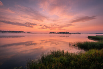 Fototapeta premium serene summer dawn unfolds over tranquil lake with soft hues of orange and pink gently illuminating horizon
