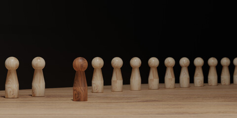 One dark wooden figure standing out among identical light wood figures on a desk. Concept of leadership, uniqueness, diversity, social identity, and inclusion.