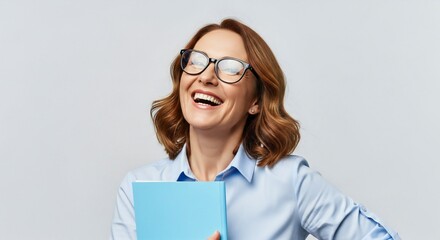 A smiling woman with glasses and wavy brown hair, wearing a blue shirt, holds a blue book against a plain light background.