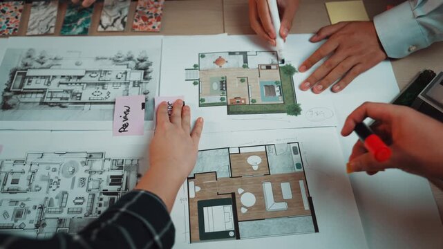 A pair of hands examining architectural blueprints and interior design plans on a workspace. Colorful samples and materials surround detailed layouts, showcasing the design process. SACTR
