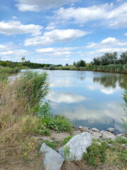 Panorama of the clear water surface of the Moskovka River, reflecting the snow-white clouds floating above it in the distance of the Zaporizhzhia steppes.