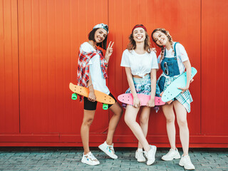 Three young smiling beautiful female with colorful penny skateboards.Women in summer hipster...