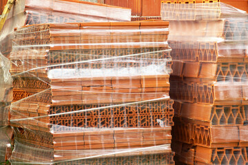 Construction materials delivery: stacked red ceramic bricks wrapped in plastic. Details from the...
