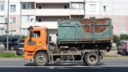 An old, rusty heavy dump truck is driving down a city street on a summer day, Tovarishchesky...
