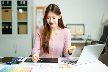Asian designer using digital pen and laptop in a creative office, showcasing professional work,...