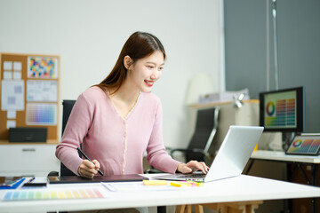 Asian designer using digital pen and laptop in a creative office, showcasing professional work,...