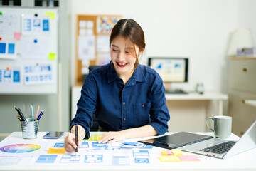 Creative designer stands at her workspace, planning UX/UI with color swatches and wireframes