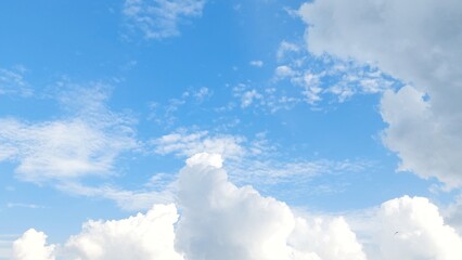 Wide view of blue sky with fluffy white clouds on a sunny day with peaceful spring ambiance background. Soft white clouds float in the clear blue sky. Clear blue sky, bright spring.