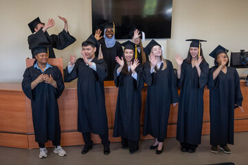 Young multinational people in graduation gowns stand at the lectern. 