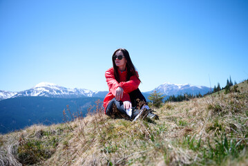 Hiker girl on background of snowy mountains. Young female in red sport jacket and sunglasses hiking...