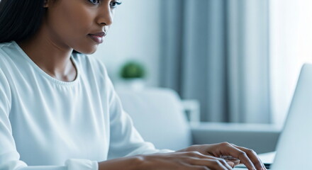 Young african american woman using laptop, focused on internet browsing or distant work in modern home office.