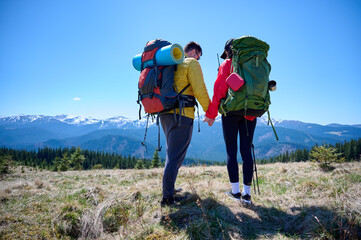 Two hikers taking a break on a mountain ridge. Sporty couple with hiking backpacks standing on...