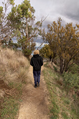 Teenage boy walks on path in Australian bush with ocean in background