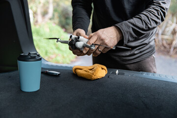 Videographer preparing drone in back of car with beanie and coffee mug