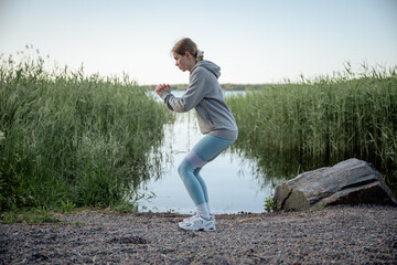woman doing resistance band squat exercise near lake in summer