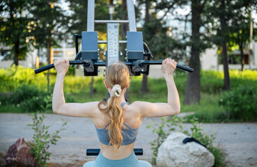 woman using lat pull down machine at outdoor gym in summer park