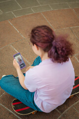 Young girl taking a selfie, sitting on a skateboard in the city