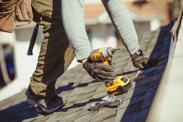 Roofer with a drill fixes a roof in a residential area