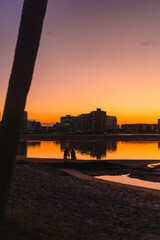 Two people silhouetted at sunset on coastal path near city skyline