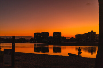 Silhouette of a person with boat, sunset on river, city background