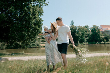 Young family walking by lake with bouquet of daisies