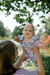 Mother lifting baby girl outdoors in summer park