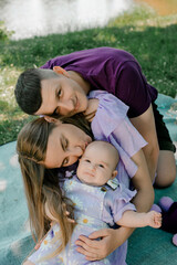Young parents cuddle baby on picnic blanket outdoors