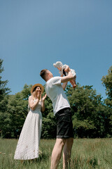 Father lifting baby girl under blue sky in summer park