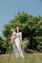 Mother with baby girl holding flowers in summer field