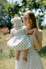 Young mother holding baby in polka dot dress outdoors