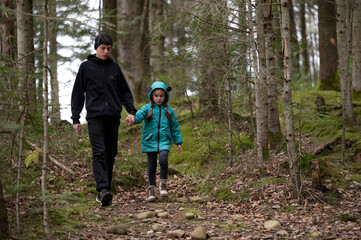 Walking through a tranquil forest path during early spring, a young boy holds hands with a girl dressed in a bright jacket as they explore nature together