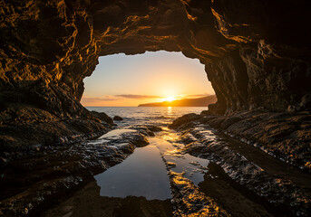 Natural rock arch formation overlooking a calm body of water at sunset