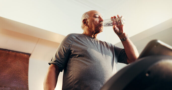 Elderly man, fitness and water with treadmill in home for workout, exercise or hydration. Active, below or senior person drinking mineral liquid on running machine for cardio break, rest or recovery