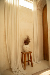 Soft curtains frame a simple vase with dried flowers on a stool