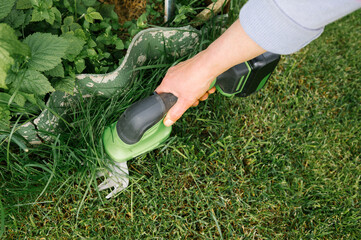 Adult caucasian hand trimming grass with electric shears in garden setting