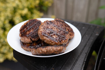 Juicy grilled beef patties on a white plate outdoors. National Mincemeat Day