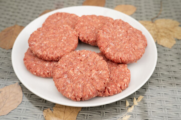 Raw beef patties on white plate with autumn leaves background. National Mincemeat Day