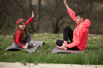 Two young individuals practicing yoga on mats in a serene outdoor setting surrounded by lush...