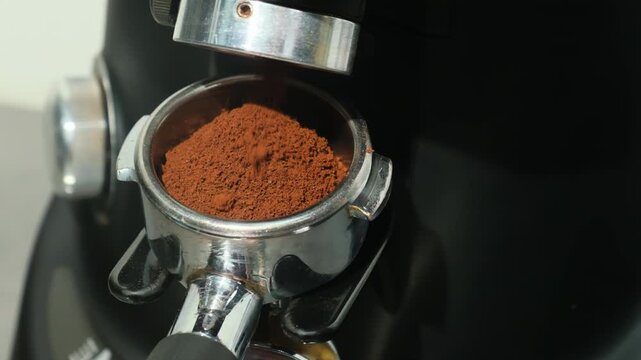 Coffee pours in thin dark stream towards metal portafilter filling device up with coffee grounds. Concept of preparing coffee slow motion