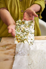 Close-up of hands holding a finished sheet of handmade floral paper with chamomile and herbs. Final result of an eco-friendly DIY papermaking process