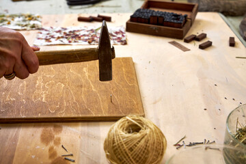 Close-up of woman hammering nails into a stained wood board for handmade decor. Part of...