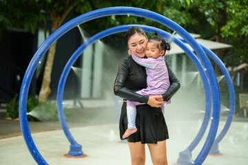happy mother with toddler girl playing water tunnel splashing in swimming pool