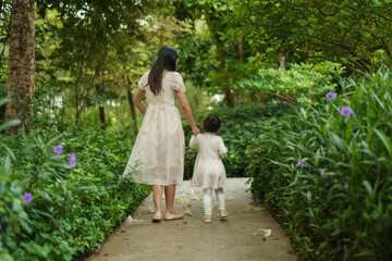mother and toddler girl in white dress walking in flower garden