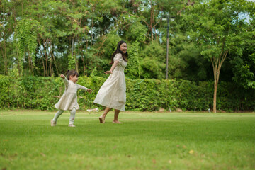 mother and toddler girl playing walk and run circling around on grass field at park