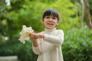 happy toddler girl in white dress with dolichandrone serrulata flower in garden