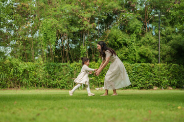 mother and toddler girl playing on grass field at park