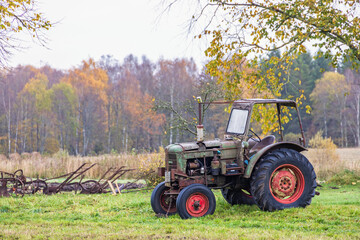 Old tractor stands on a meadow in an autumnal landscape
